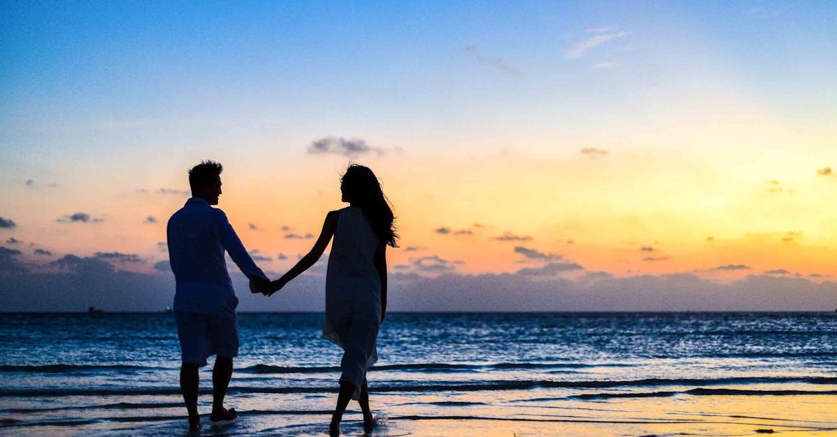 A romantic couple walks hand in hand on a tropical beach at sunset, enjoying a serene moment together.