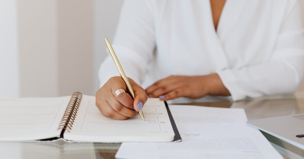 Close-up of a person writing notes in a planner with a gold pen, emphasizing organization.